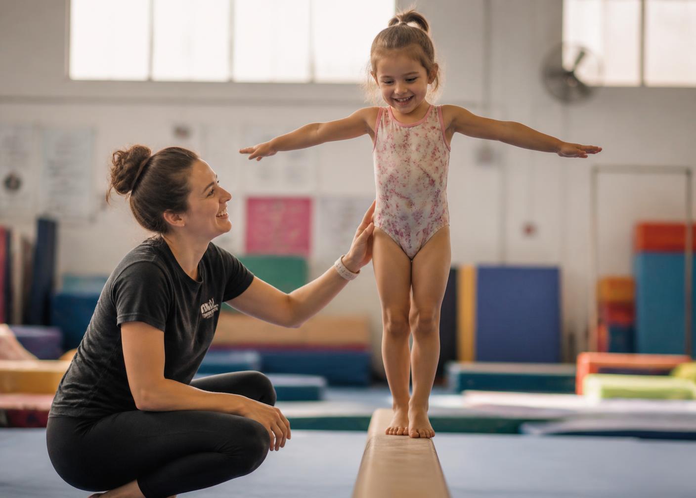 A coach spotting a young gymnast on the balance beam